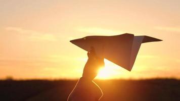mujer lanza papel avión en contra puesta de sol antecedentes. concepto de falto a Vamos en vacaciones o viajar. lento movimiento video