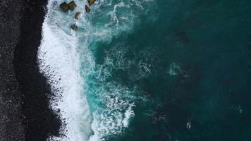 parte superior ver de un abandonado negro volcánico playa. costa de el isla de tenerife aéreo zumbido imágenes de mar olas alcanzando apuntalar video