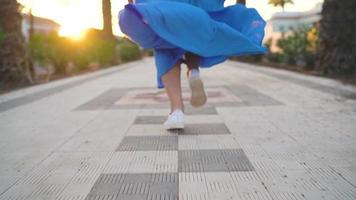 piernas de un mujer en un hermosa azul vestir corriendo a lo largo el palma avenida. sombrero caídas a el suelo. dramático lento movimiento video