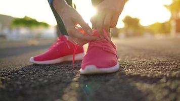 cerca arriba de mujer atadura zapato cordones y corriendo a lo largo el palma avenida a puesta de sol video