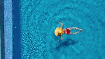 vue de le Haut comme une femme dans une rouge maillot de bain mensonge sur sa retour dans le bassin. relaxant concept video