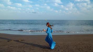 mujer en hermosa azul vestir corriendo a lo largo un negro volcánico playa video