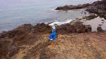 View from the height of woman in a beautiful blue dress and hat stands on top of a mountain in a conservation area on the shores of the Atlantic Ocean. Tenerife, Canary Islands, Spain video