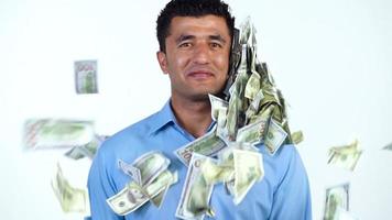 An Arab man stands on a white background, and a lot of dollar bills are suddenly thrown at him from different sides. Slow motion video