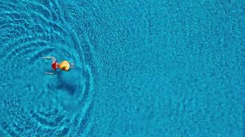 View from the top as a woman in a red swimsuit lying on her back in the pool. Relaxing concept video