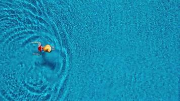 View from the top as a woman in a red swimsuit lying on her back in the pool. Relaxing concept video