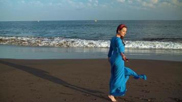 retrato de un mujer en un hermosa azul vestir en un negro volcánico playa video