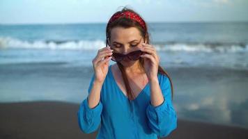 retrato de un mujer en un hermosa azul vestir en un negro volcánico playa video