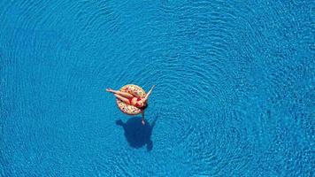 Visualizza a partire dal il superiore come un' donna nel un' rosso costume da bagno nuoto e dire bugie su sua indietro nel il piscina. rilassante concetto video