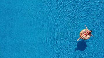 View from the top as a woman in a red swimsuit swimming and lying on her back in the pool. Relaxing concept video