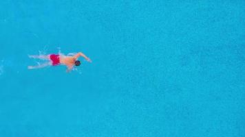 Aerial view of man in red shorts swims in the pool. Slow motion video