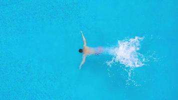 Aerial view of man in red shorts swims in the pool. Slow motion video