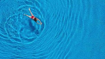 Aussicht von das oben wie ein Frau im ein rot Badeanzug Schwimmen und Lügen auf ihr zurück im das Schwimmbad. entspannend Konzept video