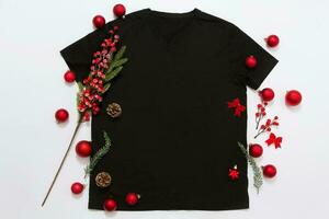 Close up black blank template t shirt with copy space and Christmas Holiday concept. Top view mockup t-shirt and red holidays decorations on white background. Happy New Year accessories. Xmas outfit photo