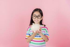 niña asiática ahorrando dinero en una alcancía, aprendiendo a ahorrar, los niños ahorran dinero para la educación futura. concepto de dinero, finanzas, seguros y personas foto