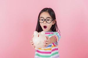 Little Asian girl saving money in a piggy bank, learning about saving, Kid save money for future education. Money, finances, insurance, and people concept photo