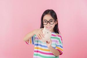 Little Asian girl saving money in a piggy bank, learning about saving, Kid save money for future education. Money, finances, insurance, and people concept photo