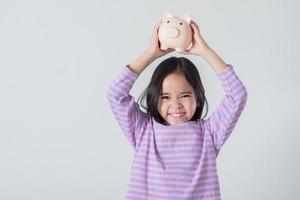 niña asiática ahorrando dinero en una alcancía, aprendiendo a ahorrar, los niños ahorran dinero para la educación futura. concepto de dinero, finanzas, seguros y personas foto