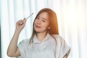 A woman in a white shirt is holding a pen and smiling. photo