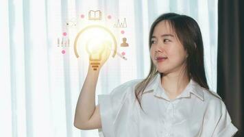 A woman is holding a lightbulb with a line of icons on the screen. photo