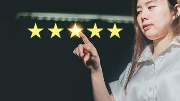 Asian woman pointing to five stars rating on dark background. Customer review concept. photo
