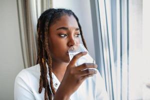 Young African woman in casualwear drinking water from glass photo