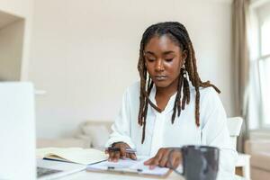 Remote job, technology and people concept - happy smiling young black business woman with laptop computer and papers working at home office photo