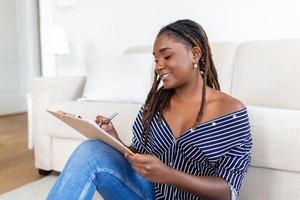 Portrait of beautiful young african woman working at home. Female sitting and writing notes. photo