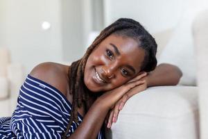 retrato de un hermosa mujer sonriente a hogar. africano mujer en casual mirando a cámara con Copiar espacio. alegre mezclado carrera niña relajante a hogar con grande reír. foto