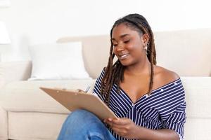 Portrait of beautiful young african woman working at home. Female sitting and writing notes. photo