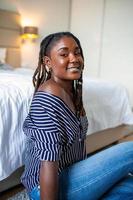 retrato de un hermosa mujer sonriente a hogar. africano mujer en casual mirando a cámara con Copiar espacio. alegre mezclado carrera niña relajante a hogar con grande reír. foto