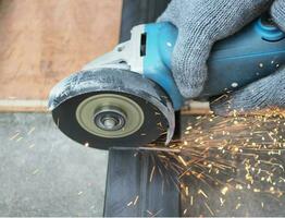 Technician using electric grinder to cut square metal pipe safely by wearing cotton gloves photo