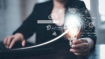 Businessman holding glowing light bulb with AI Data Management System on the computer, Hands working on a laptop cloud network graphic overlay, connected to the database. Corporate strategy finance photo