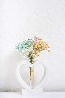 Plaster vase in the shape of a heart with multi-colored gypsophila flowers on white background photo