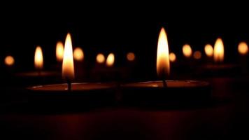 many candles burning in groups and their fire on a black background, fires of many candles moving with wind and give a soft light, selective focus video