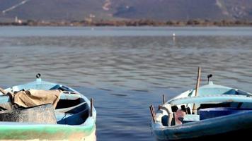 Anchored boat on shore of lake in backlighting, boats moored in marina on lake with mountain and nature view, selective focus video