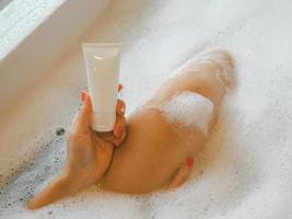 Asian woman soaking in a bathtub with a tube of skin cream. photo