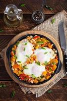 Shakshouka in frying pan. Fried eggs with vegetables, tomato, pepper, pumpkin and onion. Top view photo