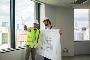 hombre ingeniero en pie en construcción sitio, participación planos foto