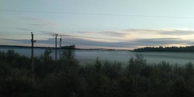 View from a moving train. Mist over the forest. Sunset sky. photo