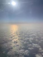 Sky travel. View from the illuminator. Fluffy white clouds. Sunlight pink and yellow reflexion on the water. Blue sky background. photo