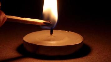 Lighting candle with a black background, candle burning with a match on a black background and gives light with fire around, selective focus video