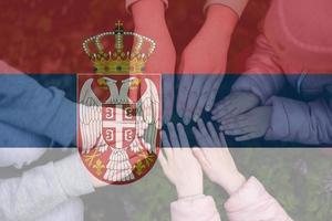 Hands of kids on background of Serbia flag. Serbian patriotism and unity concept. photo