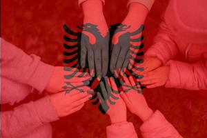 Hands of kids on background of Albania flag. Albanian patriotism and unity concept. photo