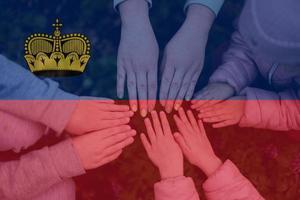Hands of kids on background of Liechtenstein flag. Liechtensteiner patriotism and unity concept. photo