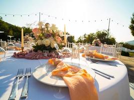 Beautiful outdoor wedding decoration in city. Candles and dried flowers and accessories with bouquets and glasses on table with linen tablecloth on newlywed table on green lawn photo