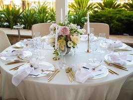 Boda banquete concepto. sillas y redondo mesa para huéspedes, servido con cuchillero y, flores y vajilla y cubierto con un Manteles foto