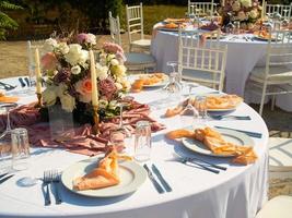 Beautiful outdoor wedding decoration in city. Candles and dried flowers and accessories with bouquets and glasses on table with linen tablecloth on newlywed table on green lawn photo