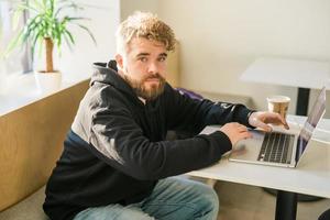 Male guy resting in coffee shop chatting in social networks skilled freelancer enjoying remote job typing publication for web blog on laptop photo