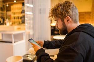 Portrait happy guy making money transaction via application on mobile phone with 4g internet sitting at cafe in street evening, serious millennial man reading text message on smartphone photo